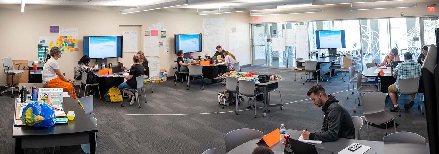 Instructor sitting on desk while students are working on projects.